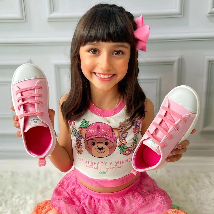 Na imagem temos uma linda menina segurando o têsnis infantil feminino Ortopé
