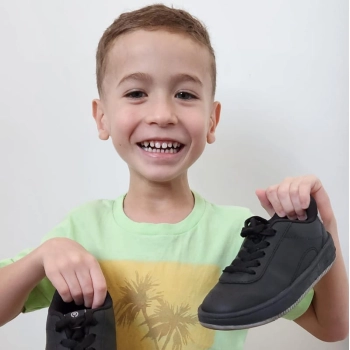 Na foto o menino vitor segura um tenis preto ortope